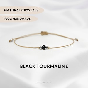 May include: A simple bracelet featuring a black tourmaline gemstone bead and silver spacer beads on a beige cord. The bracelet is adjustable and has a sliding knot closure. The text "NATURAL CRYSTALS 100% HANDMADE" is displayed above the bracelet and "BLACK TOURMALINE" is displayed below the bracelet. The text "YPCRYSTALJEWELRY" is displayed at the bottom of the image.
