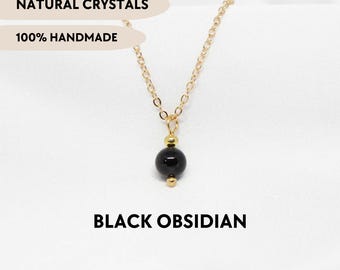 May include: A gold-toned chain necklace featuring a single spherical black obsidian bead pendant accented by two small gold-toned metal beads. The image includes the text NATURAL CRYSTALS, 100% HANDMADE, BLACK OBSIDIAN, and YPCRYSTALJEWELRY.