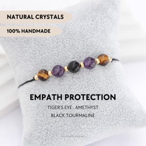 Puede incluir: Una pulsera hecha a mano con cuentas de ojo de tigre, amatista y turmalina negra. La pulsera está ensartada en un cordón negro y acentuada con cuentas doradas. Se muestra el texto "Empath Protection".