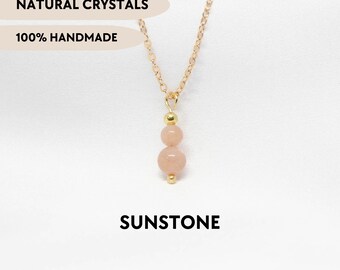 May include: A gold-toned chain necklace featuring a pendant with two round, peach-coloured sunstone beads separated by a small gold-toned bead. The text NATURAL CRYSTALS, 100% HANDMADE, and SUNSTONE is visible on the image along with YPCRYSTALJEWELRY.
