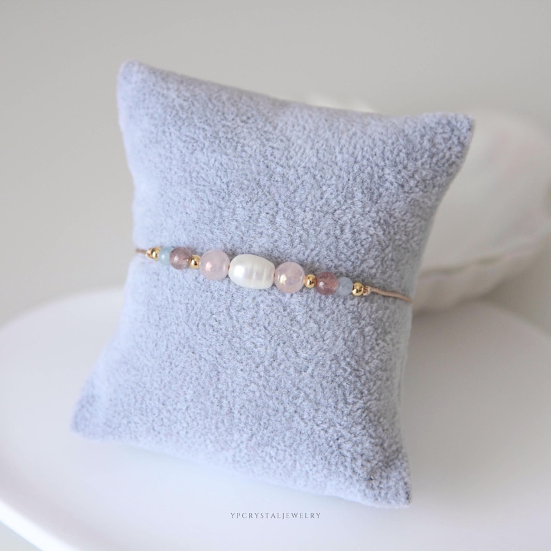 May include: A delicate bracelet featuring a central white oval pearl flanked by light pink and translucent beads, accented with small gold-toned metallic spheres on a thin cord. The text YPCRYSTALJEWELRY is printed at the bottom of the image.