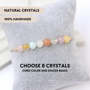 Puede incluir: Una pulsera delicada con ocho cuentas de cristal natural lisas, redondas y multicolores ensartadas en un cordón fino. El texto en la imagen dice: NATURAL CRYSTALS, 100% HANDMADE, CHOOSE 8 CRYSTALS, CORD COLOR AND SPACER BEADS.