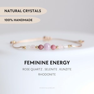 Può includere: Un braccialetto fatto a mano con cristalli naturali, tra cui quarzo rosa, selenite, kunzite e rodonite. Il braccialetto è infilato su un cordoncino beige con perline dorate. Il testo recita "FEMININE ENERGY".