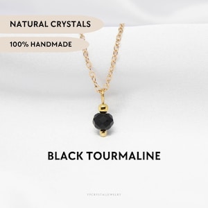 Puede incluir: Un collar de cadena dorada con una cuenta de turmalina negra facetada centrada entre dos pequeñas esferas doradas. La imagen incluye el texto NATURAL CRYSTALS, 100% HANDMADE, BLACK TOURMALINE y el nombre de la marca YPCRYSTALJEWELRY.