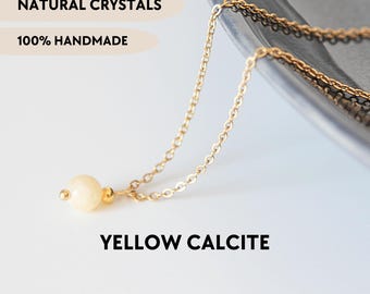 May include: A gold-toned chain necklace featuring a single, round, pale yellow calcite bead. The image includes the text NATURAL CRYSTALS, 100% HANDMADE, YELLOW CALCITE, and YPCRYSTALJEWELRY. The design consists of a delicate metal link chain.