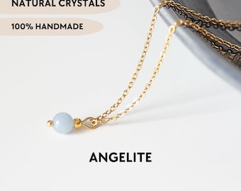 May include: A gold-toned chain necklace featuring a single round, pale blue Angelite crystal bead. The text NATURAL CRYSTALS, 100% HANDMADE, ANGELITE, and YPCRYSTALJEWELRY are visible. The delicate metal chain links are connected to the bead with a small gold-toned finding.