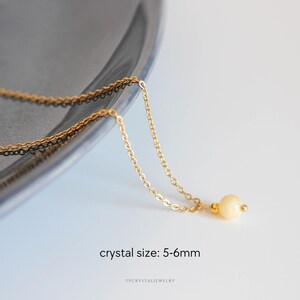 Puede incluir: Un collar de cadena en tono dorado con un colgante de una sola cuenta de cristal redonda de color amarillo p&aacute;lido. La cuenta est&aacute; acentuada por un peque&ntilde;o espaciador de metal dorado. El texto "crystal size: 5-6mm" y "ypcrystaljewelry" aparece debajo.