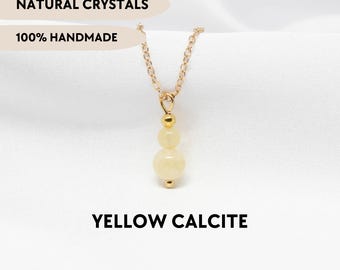 May include: A gold-toned chain necklace featuring a pendant with two stacked, smooth, pale yellow calcite beads and a small gold-toned spacer bead. The image includes the text NATURAL CRYSTALS, 100% HANDMADE, YELLOW CALCITE, and YPCRYSTALJEWELRY.