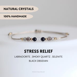 Puede incluir: Una pulsera delicada con cuentas de cristales naturales de labradorita, cuarzo ahumado, selenita y obsidiana negra, intercaladas con pequeñas cuentas metálicas doradas en un cordón beige. Texto: NATURAL CRYSTALS, 100% HANDMADE, STRESS RELIEF, LABRADORITE, SMOKY QUARTZ, SELENITE, BLACK OBSIDIAN, YPCRYSTALJEWELRY.