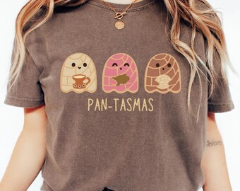 Könnte beinhalten: Ein braunes T-Shirt mit dem Text "PAN-TASMAS" unter drei Cartoon-Brotfiguren. Die Brotfiguren sind in den Farben Beige, Rosa und Braun gehalten. Einer hält eine Kaffeetasse, ein anderer hat eine Füllung und der letzte hält ein Brotstück.