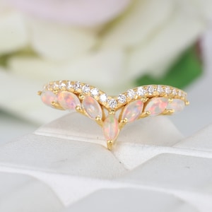 May include: A gold ring with a V-shaped design featuring a row of small clear stones and a row of larger pear-shaped opal stones.