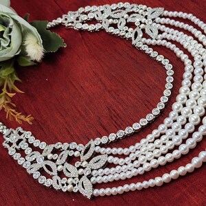May include: A silver necklace with a multi-layered pearl strand and a large, ornate, crystal-encrusted pendant.