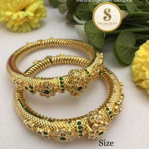 May include: Two gold-colored Jadau openable bangles. The bangles feature intricate detailing with white and green gemstones. The text "Jadau Openble bangles" and "Size 24/6/8" are visible.