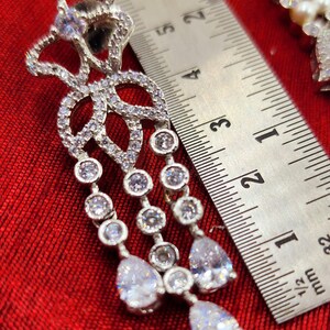 May include: Silver dangle earrings with a floral design and clear cubic zirconia stones. The earrings are approximately 2 inches long.