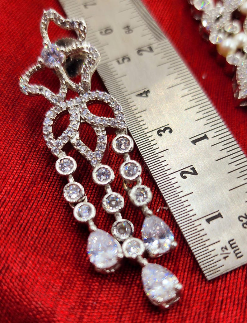 May include: Silver dangle earrings with a floral design and clear cubic zirconia stones. The earrings are approximately 2 inches long.