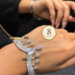 Könnte beinhalten: Ein silberfarbenes Armband mit einem zentralen rechteckigen, klaren Stein und kleineren, tropfenförmigen, klaren Steinen. Das Armband ist mit mehreren funkelnden Steinen besetzt. Der Text "DDL" und "PREMIUM QUALITY" sind sichtbar.