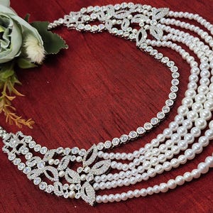 May include: A silver necklace with a multi-layered pearl strand and a large, ornate, crystal-encrusted pendant.