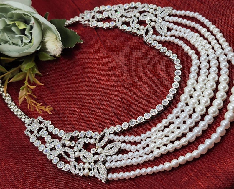 May include: A silver necklace with a multi-layered pearl strand and a large, ornate, crystal-encrusted pendant.