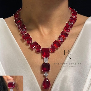 Può includere: Una collana e orecchini con grandi pietre preziose rosse. La collana presenta una serie di pietre rosse rettangolari e a goccia, con pietre trasparenti più piccole. Gli orecchini riprendono il design della collana. Il testo "HK PREMIUM QUALITY Feel Like a Diamond" è incluso.