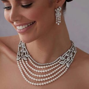 May include: A multi-strand pearl necklace with a diamond and pearl pendant. The necklace is made of white pearls and has a silver-toned metal clasp.