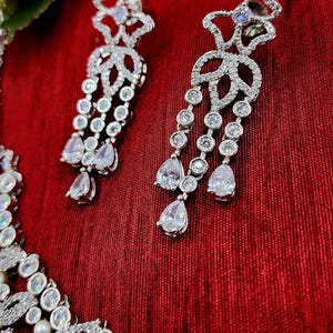 May include: A silver necklace with a pearl and crystal design, paired with matching crystal earrings. The necklace features a floral motif and the earrings are long and dangle.