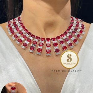 Op de afbeelding: Een opvallende ketting en bijpassende oorbellen met heldere rode en witte edelstenen. De ketting heeft ovale rode stenen en rechthoekige witte stenen. De oorbellen volgen dit ontwerp. De afbeelding bevat de tekst "Daily Designs By Senti".