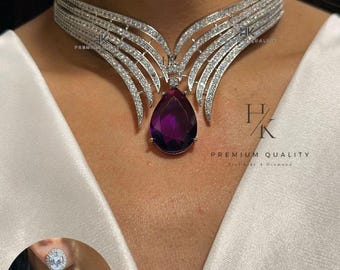 May include: A dazzling silver-toned necklace and matching earrings. The necklace features a wide collar design with a central teardrop-shaped, deep purple gemstone pendant. The earrings mirror the necklace's design, with a purple gemstone at the base. The text "PREMIUM QUALITY" is visible.