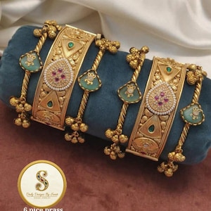 May include: Six brass heritage bangles with detailed gold patterns, adorned with turquoise teardrop shapes and gemstones. The bangles are presented on a teal cushion. The image includes the text "6 pice brass Heritage bangles Size 2.2/2.4/2.6/2.8".
