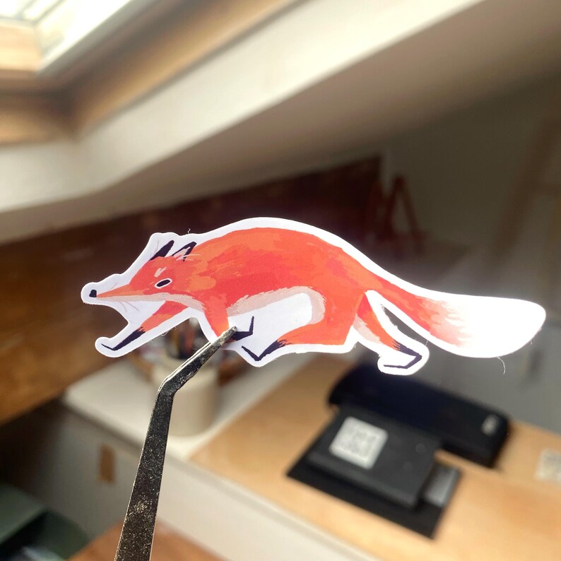 May include: A red fox sticker with a white background. The fox is running and has a long tail.