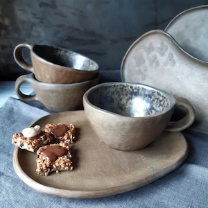 Può includere: Set di stoviglie in ceramica fatte a mano nei toni del marrone e del grigio. Il set comprende due tazze da caffè, un piattino e un vassoio da portata. Le tazze hanno una forma unica e un interno strutturato. Perfetto per caffè o tè.