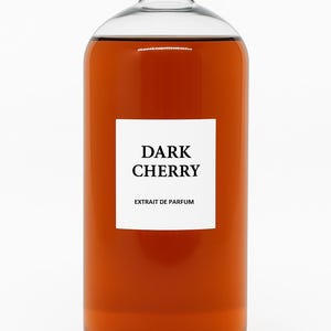 Op de afbeelding: Een heldere glazen fles met een zilveren deksel gevuld met een donker amberkleurige vloeistof. De fles heeft een wit etiket met de tekst "DARK CHERRY" en "EXTRAIT DE PARFUM" in zwarte letters.