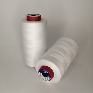 Op de afbeelding: Twee spoelen witte Coats Epic draad met rode en blauwe etiketten. Het etiket op de spoel op de voorgrond luidt "COATS Epic 23/8 100% POLYESTER 2250 YARDS (2050 METERS)".