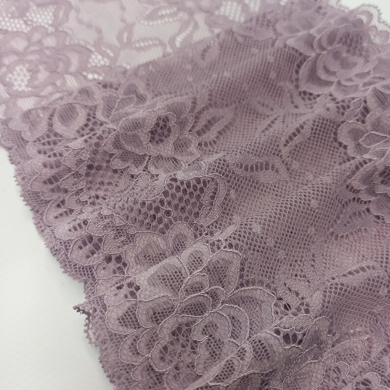 May include: A close-up of a delicate, mauve-colored lace fabric with a floral pattern. The lace is soft and flowing, with a delicate texture.