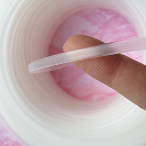 Puede incluir: Primer plano de una moldura de pl&aacute;stico flexible, blanca y transl&uacute;cida. La moldura est&aacute; siendo sostenida por un dedo, mostrando su flexibilidad.
