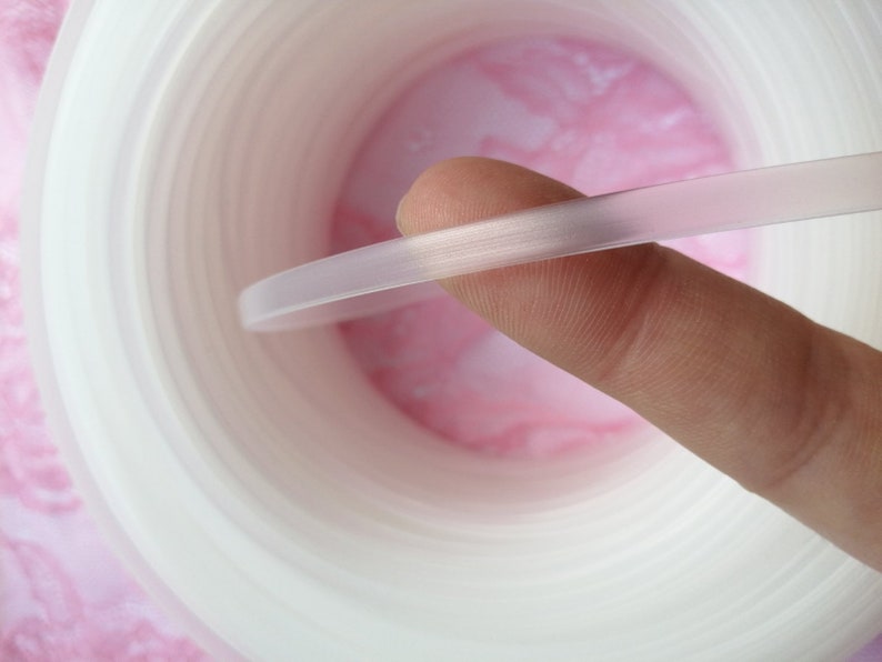 Puede incluir: Primer plano de una moldura de pl&aacute;stico flexible, blanca y transl&uacute;cida. La moldura est&aacute; siendo sostenida por un dedo, mostrando su flexibilidad.