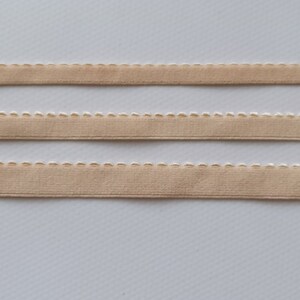 May include: Three pieces of beige elastic trim with a white scalloped edge.