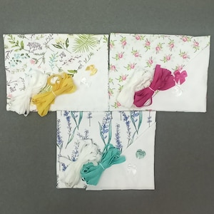 May include: Three fabric squares with different floral patterns, each with white lace trim, ribbon, and a small white bow. The ribbons are yellow, pink, and teal.