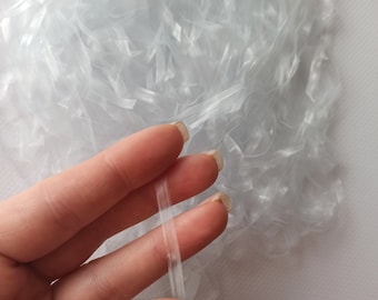 May include: A pile of white, thin, plastic fibers. A hand is holding a few strands of the fiber.