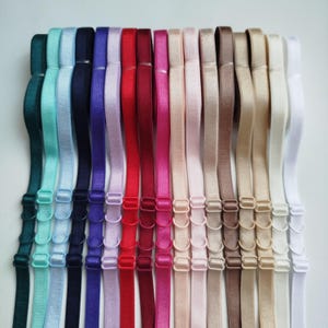 以下が含まれることがあります： さまざまな色合いのカラフルなブラストラップのコレクション。ティール、ネイビー、パープル、レッド、ベージュなど。各ストラップには、長さ調整用の調節可能な金属製ハードウェアが付いています。ストラップは白い背景に対して垂直に配置されています。