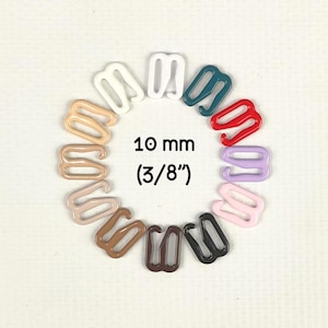 Puede incluir: Un conjunto de doce ajustadores de tirantes de sujetador de metal dispuestos en círculo, con varios colores que incluyen blanco, verde azulado, rojo, lavanda, rosa, negro, marrón y beige. El texto 10 mm (3/8") está impreso en el centro.