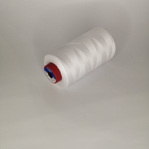 Pu&ograve; includere: Un'bobina di filo bianco con un'etichetta rossa e blu. L'etichetta dice "COATS" e "100% Poliestere".