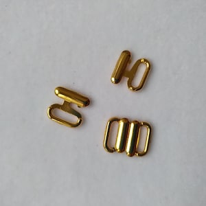 Puede incluir: Tres cierres de metal dorado para tirantes de sujetador. Los cierres son de diferentes formas y tamaños.