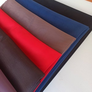 May include: A collection of folded fabric swatches in various solid colors including black, navy blue, brown, and bright red. Each piece of fabric features a fine, ribbed texture running diagonally across the surface of the material.