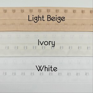 May include: Image showing three rows of hook and eye closures in light beige, ivory, and white. The text "Light Beige", "Ivory", and "White" are displayed below each respective row. These closures are used in clothing.
