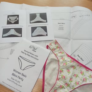 May include: A sewing pattern for a basic bikini panty with step-by-step instructions. The pattern is for sizes XS-3XL and is labeled as an initial difficulty level. The pattern is shown next to a white bikini panty with a pink trim and a floral print.