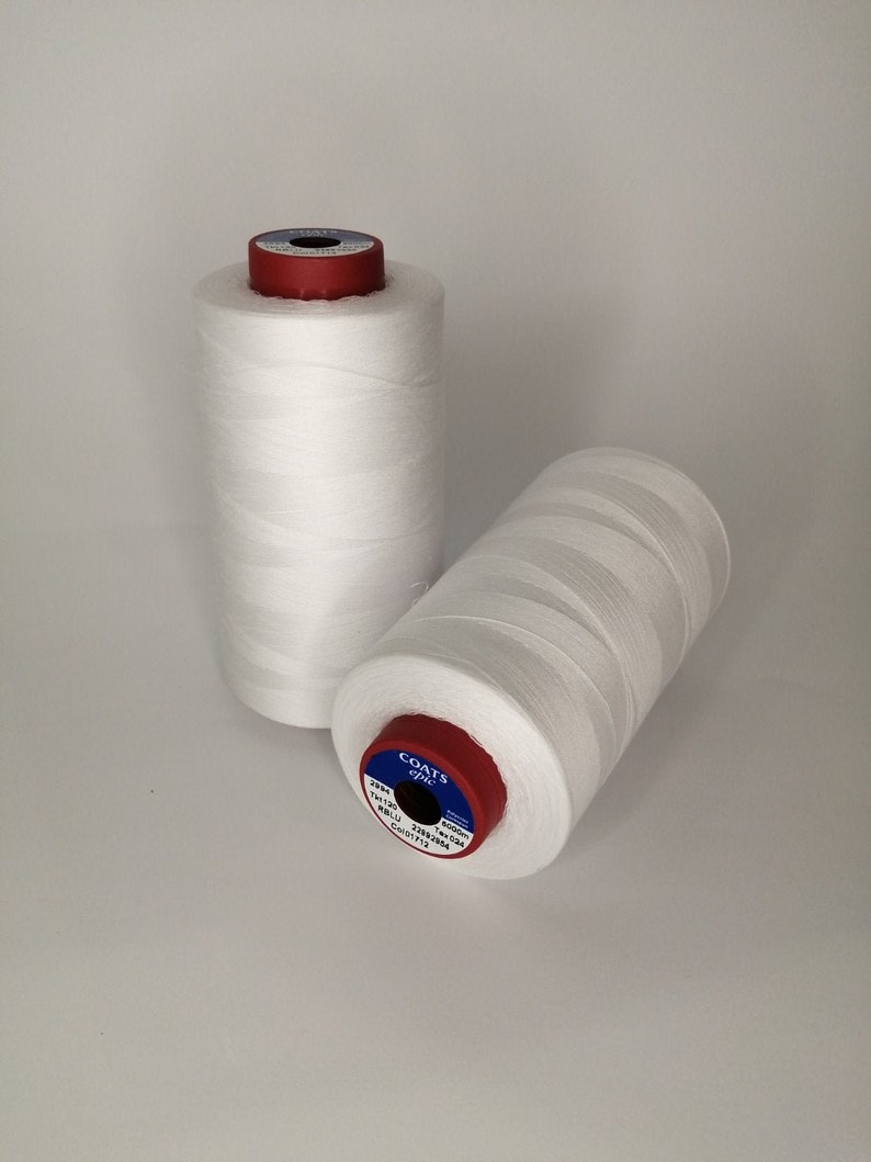 Pu&ograve; includere: Due bobine di filo bianco Coats Epic con etichette rosse e blu. L'etichetta sulla bobina in primo piano recita "COATS Epic 23/8 100% POLYESTER 2250 YARDS (2050 METERS)".