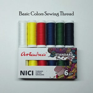 以下が含まれることがあります： 白、黄、赤、青、緑、濃い青の6つのスプールからなる、Ariadna Standardミシン糸のセットです。パッケージには「NICI」と「6 sztuk pcs」のラベルが貼られています。