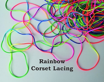 Puede incluir: Cordones de colores arcoíris para el lazado de corsé. Los cordones están dispuestos en una pila enredada.