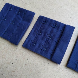 May include: Three navy blue bra extenders with metal hooks. Each extender has three rows of hooks.