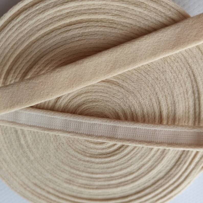 Puede incluir: Primer plano de un rollo de cinta el&aacute;stica beige con una banda el&aacute;stica blanca en la parte superior. La cinta es suave y el&aacute;stica, perfecta para a&ntilde;adir un toque de elegancia a cualquier proyecto.